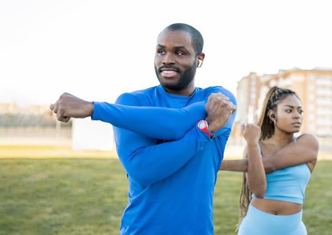 Couple standing outside, doing shoulder stretches?