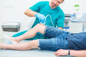 Doctor using musculoskeletal ultrasound on patient’s knee