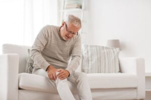 Senior man sitting on sofa, experiencing knee pain 